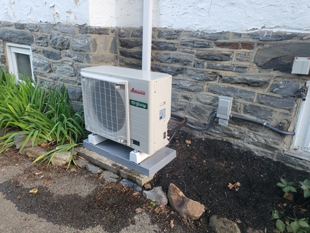 Amana/McGinley HVAC heat pump unit sits outdoors on a concrete slab